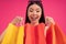 Image of joyous young asian woman expressing surprise and holding colorful paper shopping bags isolated over pink background.