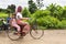 Image of a Khmer rural women in the countryside riding bike with child. Traditional clothes and rural scene.