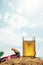 Image of light foamy beer, glass standing into sand over sea and sky background. Summertime chill. Beer bubbles