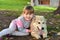 Image of little girl hugging white puppy dog laying on park ground