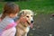 Image of little girl touching white puppy dog laying on park ground