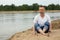 The image lonely positive man sitting on the beach river