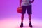 Image of low section of biracial basketball player with basketball on neon purple background