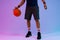 Image of low section of biracial basketball player with basketball on purple to blue background