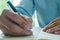 Image of male hand focusing holding a pen to write.  Businessman writing on paper report in office