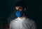 Image of a man wearing medical blue mask using smart phone during virus epidemic lockdown on black background. Caucasian male with