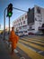 In the image, a monk waits calmly at a traffic light, his serene presence a peaceful contrast to the busy cityscape around him