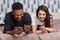 Image of multiracial couple use modern smart phones and wireless internet connection, satisfied with networking via cellular, lie