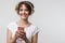 Image of optimistic woman in basic t-shirt holding smartphone while listening to music with headphones