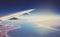 Image of plane and wing with sea, mountains, and coastline. Horizont line and sunrise.