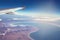 Image of plane and wing with sea, mountains, and coastline. Horizont line and sunrise.