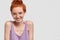 Image of pleasant looking ginger girl with gentle toothy smile, poses against white background, dressed in casual t