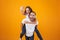 Image of pleased couple having fun while man piggybacking cute woman, isolated over yellow background