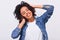 Image of pleased dark-skinned young woman dressed in blue shirt, holding hands on head, feels happy. African American female