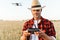 Image of pleased handsome man using drone while standing at cereal field