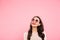 Image of pleased happy adult girl with red lips wearing round sunglasses looking upward on copy space, isolated over pink