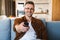 Image of pleased man smiling and using remote control while watching tv