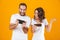 Image of pleased man and woman playing together video games on smartphones, isolated over yellow background