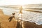 Image of pleased woman 20s running with her dog, by seaside in the morning