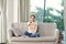 Image of a positive smiling optimistic young woman sit indoors at home watch tv holding remote control on sofa