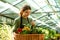 Image of pretty florist woman 20s wearing apron carrying basket with plants