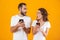 Image of puzzled couple man and woman using smartphones together, isolated over yellow background