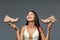 Image of a puzzled shopaholic brunette woman in underwear, holding new shoes, shows emotions, on a gray background.