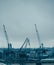 Image of river, floating cranes, buildings on river bank.