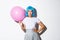 Image of sassy asian woman in blue wig, looking determined, holding pink balloon, standing over white background