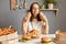 Image of satisfied cheerful young adult Caucasian woman wearing white casual T-shirt sitting at table in kitchen, holding in hands