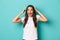 Image of scared and alarmed brunette girl in white t-shirt, shouting and holding hands over head, standing in panic over