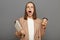 Image of shocked despair Caucasian brown-haired woman wearing jacket holding clipboard with documents and take away coffee, posing