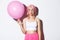 Image of silly party girl with bright makeup, pink wig, holding big cute balloon and pouting, standing over white