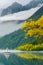 image of a small sail boat in the serene lake with trees and plants in spring colors around by foggy mountains.