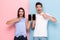 Image of smiling man and woman in casual wear standing and holding cell phones, isolated over colorful background