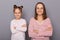 Image of smiling satisfied delighted woman and little girl with hair buns wearing casual clothes, standing with crossed hands,