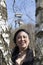 Image of a smiling woman in the middle of two tree trunks with a tower of a mine background