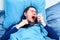 Image of sneezing sick man in scarf and with handkerchiefs in hand lying in bed .