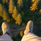 image of someone sitting on high area with bird\\\'s eye view looking down on the landscape below with a pair of legs in view