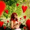 The image in the style of fantasy Valentine\'s Day. Young beautiful girl knits red hearts that fly around it.