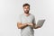 Image of surprised male model in glasses and gray t-shirt, looking amazed, using laptop, standing over white background