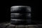 Image of three black vehicle tires stacked vertically on top of each other against a white background., New tires pile on a dark