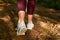 Image of woman`s legs going on ground in field or forest, woman walking along dusty road in maroon leggins and gray sneakers,