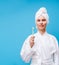 Image of woman in white coat and towel on her head with toothbrush in her hand