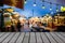 Image of wooden table in front of decorative outdoor string lights bulb in night market with blur people