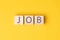 Image of the word JOB on wooden cubes on a yellow background. Concept of job search, employment, hiring or career within
