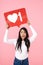 Image of young brunette asian woman holding heart like symbol on placard