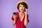 Image of young brunette woman 20s in straw hat and earphones listening to music on smartphone, isolated over violet background