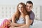 Image of young couple, curly haired wonan and habdsome man, sit in bed, embrace each other and have pleasant talk, looking