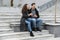 Image of young satisfied man and woman 20s in warm clothes, drinking takeaway coffee while sitting on bench outdoor